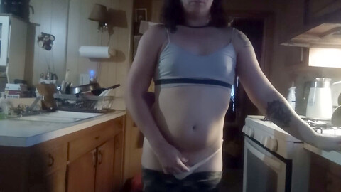 Une transsexuelle sexy se déshabille dans son petit string jaune tout en faisant la vaisselle et en fumant.